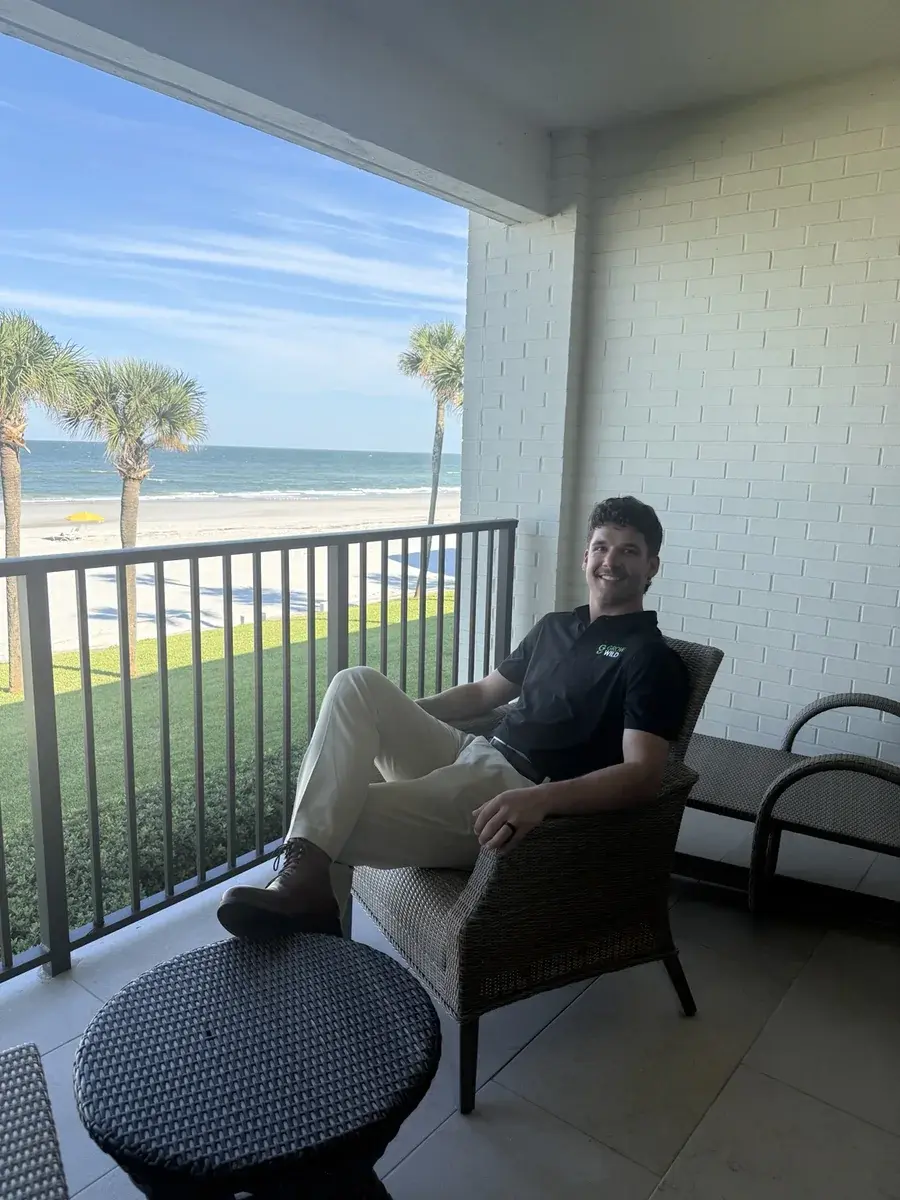 Kaden Ewald in a Grow Wild polo, seated on a balcony overlooking the beach.